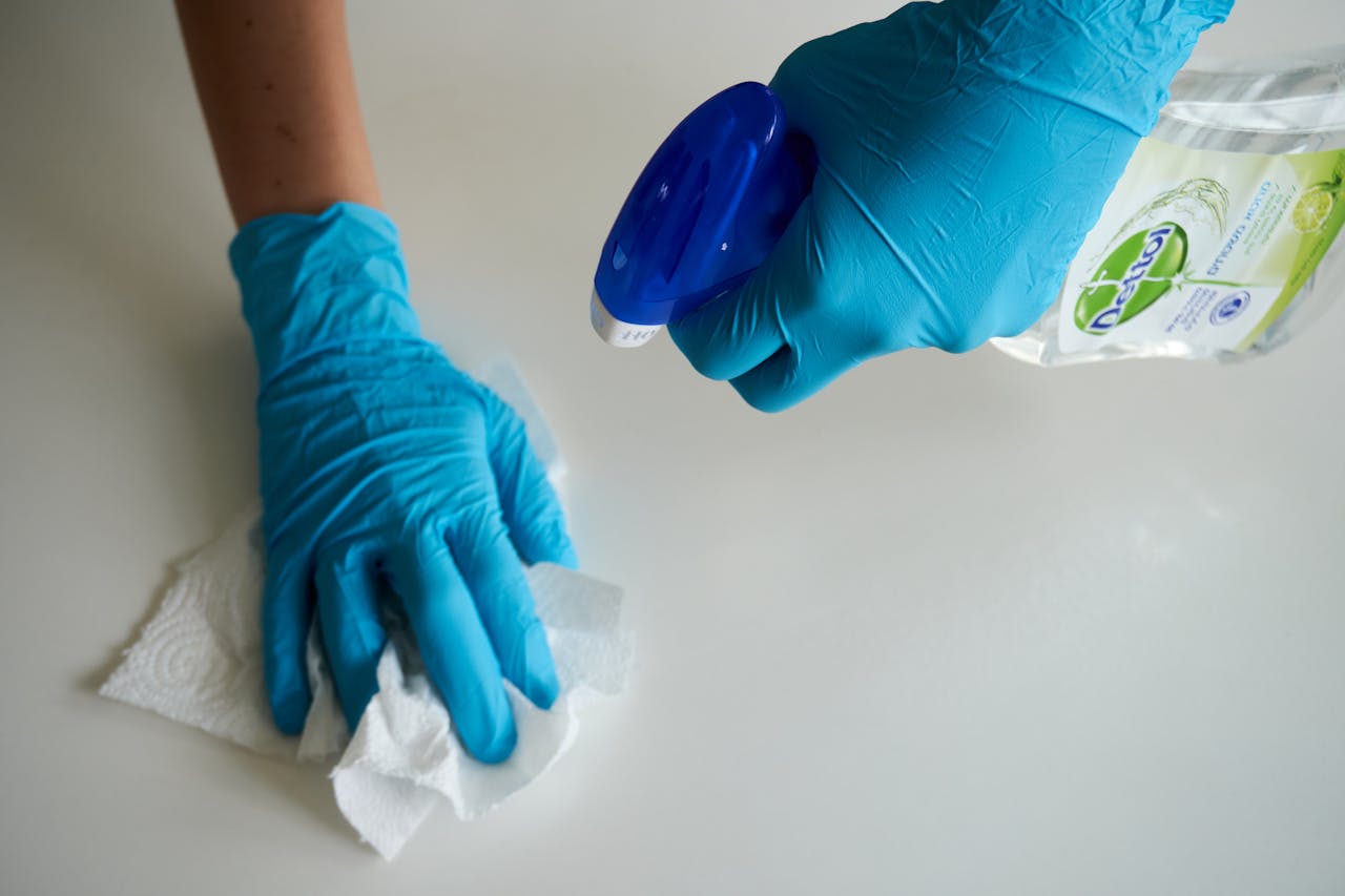 contact-img Close-up of hands wearing gloves cleaning a surface with disinfectant spray.